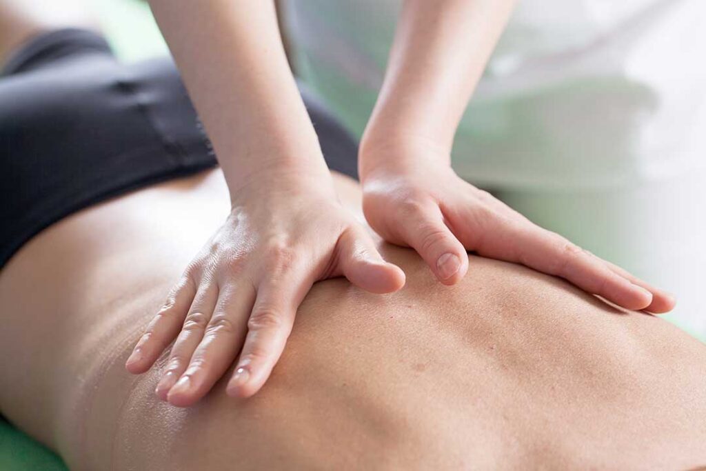 A chiropractor gently examining a patient's back in a bright clinical office setting.