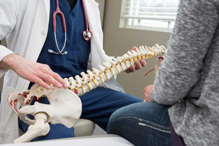Person applying a wrapped cold pack to the lower back while seated on a couch.